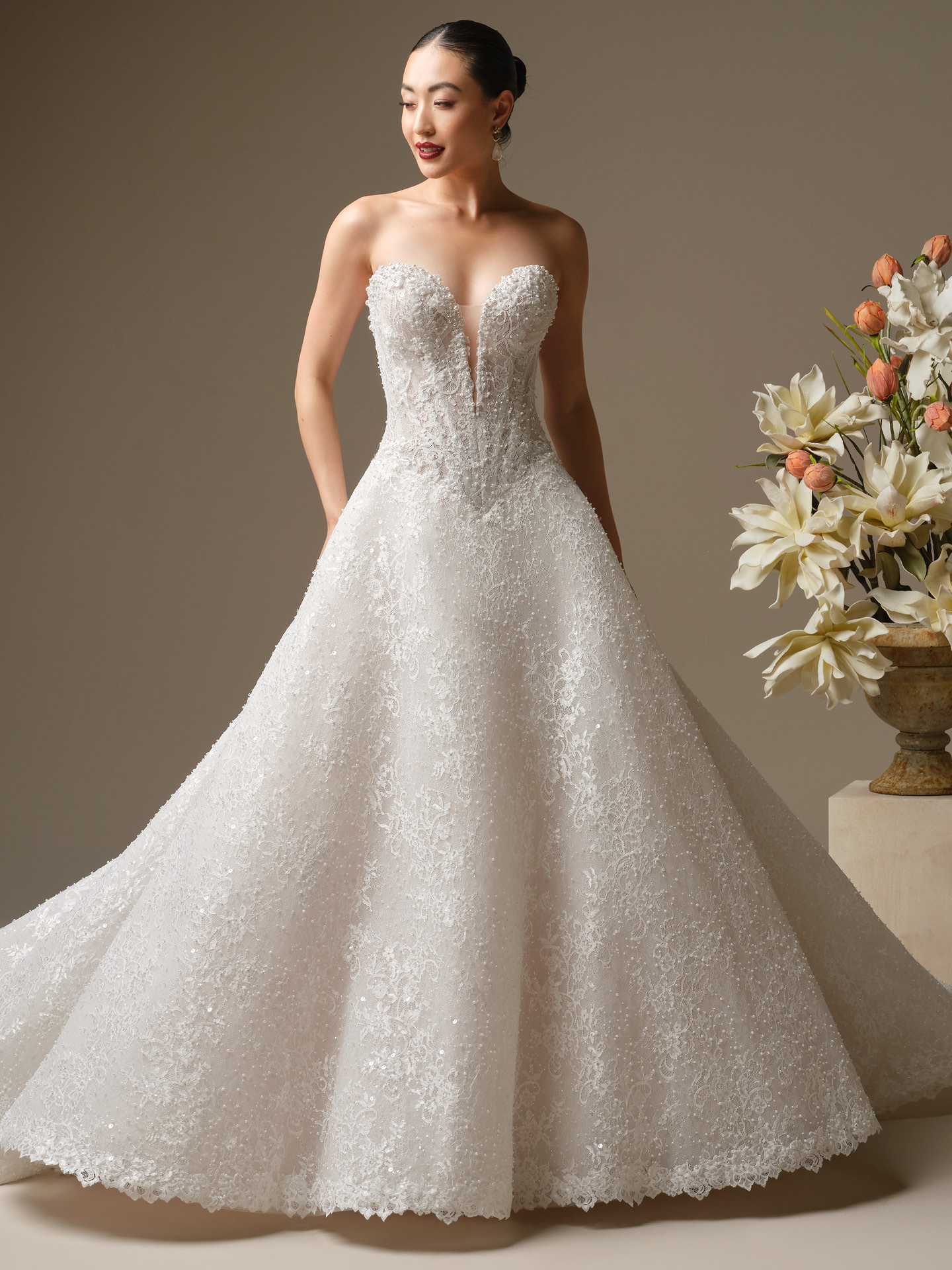 Bride wearing Angelica by Sottero and Midgley, a strapless A-line wedding dress featuring a plunging illusion sweetheart neckline, beaded lace appliqué throughout, a fitted bodice, and a full glittering skirt with a soft sweeping train.