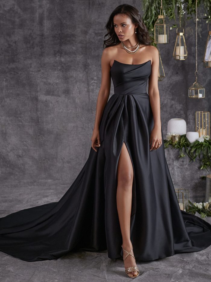 Bride wearing Aspen by Sottero and Midgley, a strapless black A-line wedding dress with draped satin bodice, thigh-high slit, and flowing train.
