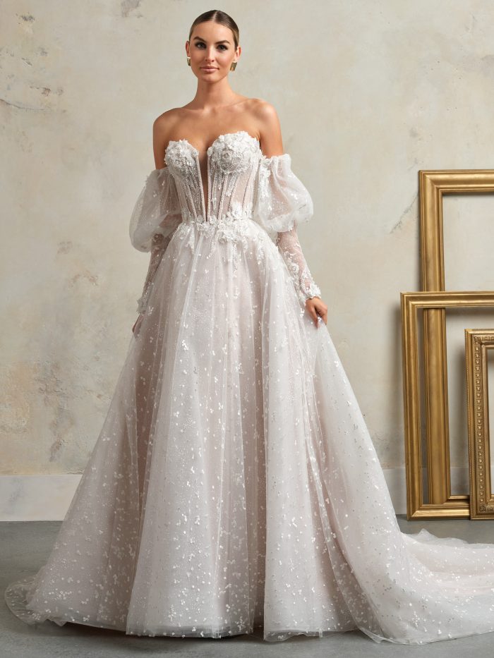 Sottero and Midgley Athlone A-line wedding dress featuring a sheer corset bodice with 3D floral appliqués, pearl beading, detachable puff sleeves, and a sparkling tulle ballgown skirt.
