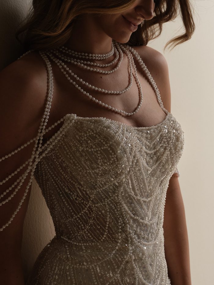 Close-up of the Constance sheath wedding dress showing intricate pearl and sequin embellishments, a strapless neckline, and layered pearl strands draped across the shoulders for a glamorous vintage-inspired look.