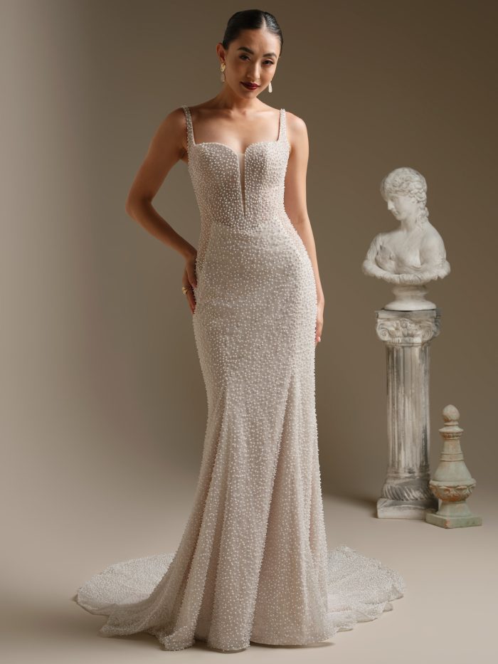 Model wearing the Cooper sheath wedding dress, designed with pearl-encrusted beading from straps to hem, a structured sweetheart bodice, and a soft flared train for a sleek, modern bridal look.