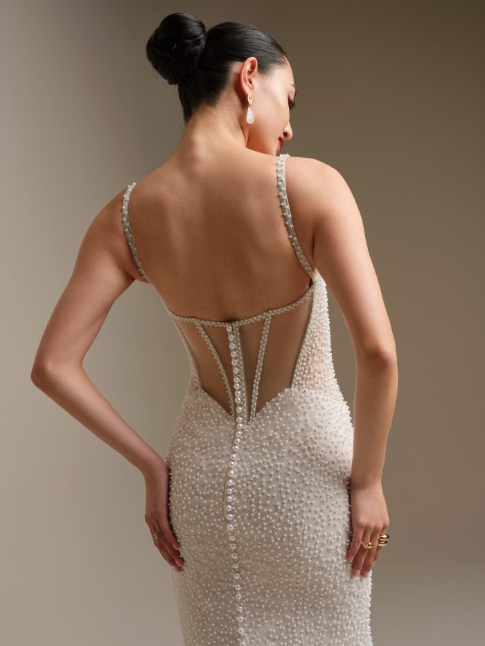 Back view of the Cooper sheath wedding dress showcasing the pearl-detailed illusion back, delicate beaded straps, and a row of pearl buttons trailing down the skirt.