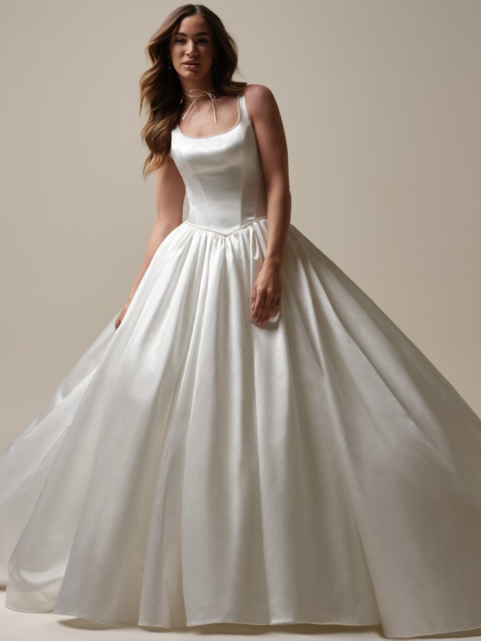 Bride wearing the Diaz ballgown wedding dress featuring a lustrous satin fabric, soft scoop neckline trimmed with pearls, and a full gathered skirt for a timeless, elegant look.