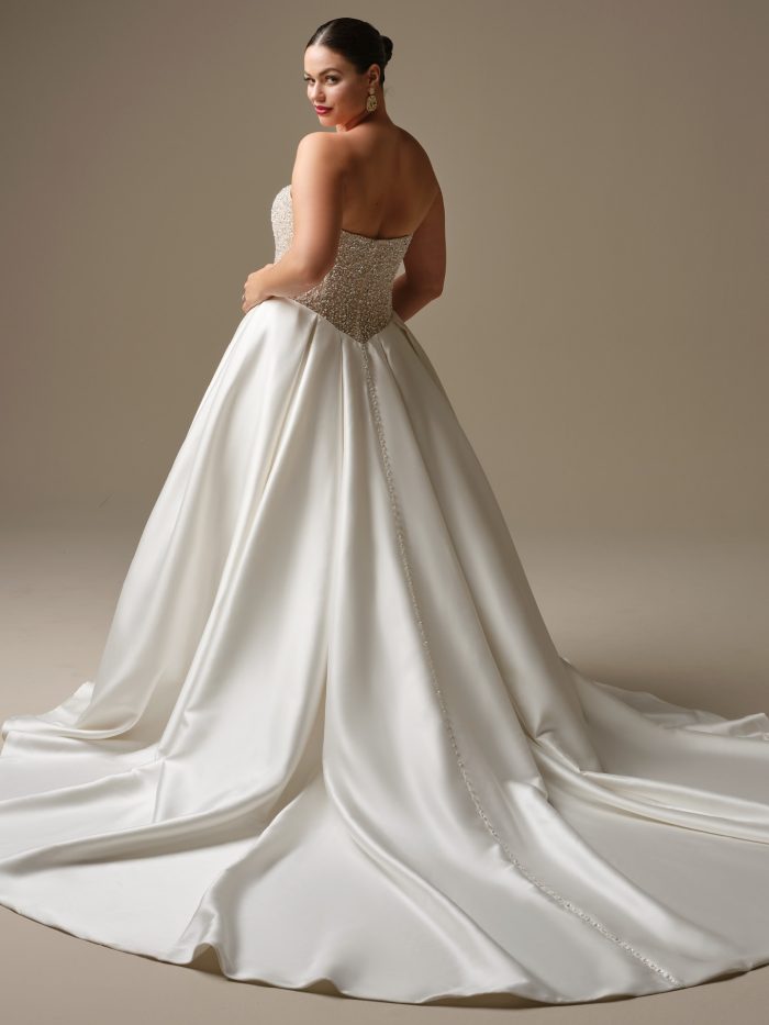 Back view of Dmara by Sottero and Midgley — plus-size satin ballgown wedding gown featuring beaded bodice, covered buttons along the back, and dramatic chapel-length train.