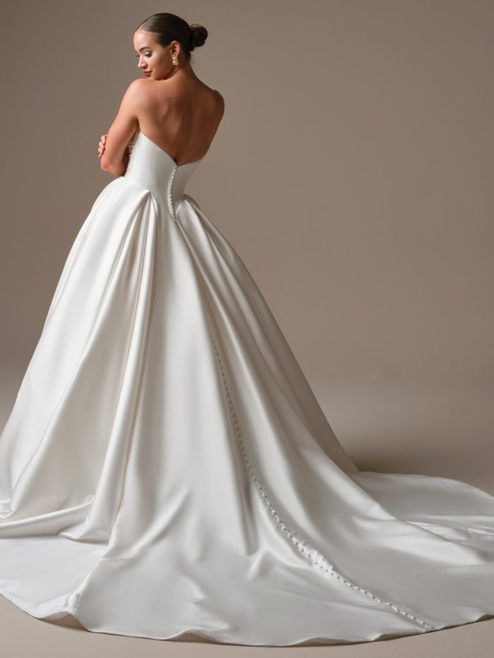 Back view of the Elias ball gown wedding dress showing the low scoop back, satin-covered buttons trailing down the train, and the gown’s structured pleated skirt.