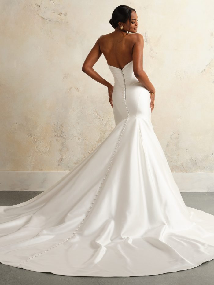 Back view of the Sottero and Midgley Giselle bridal gown showing the curved V-back, zipper closure, and a line of covered buttons trailing to the hem over the extended satin train.