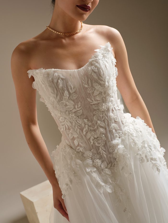 Close-up of the Jayna wedding dress highlighting the cat-eye neckline, sheer corset bodice with 3D floral appliqués, and textured lace details cascading into the pleated tulle skirt.