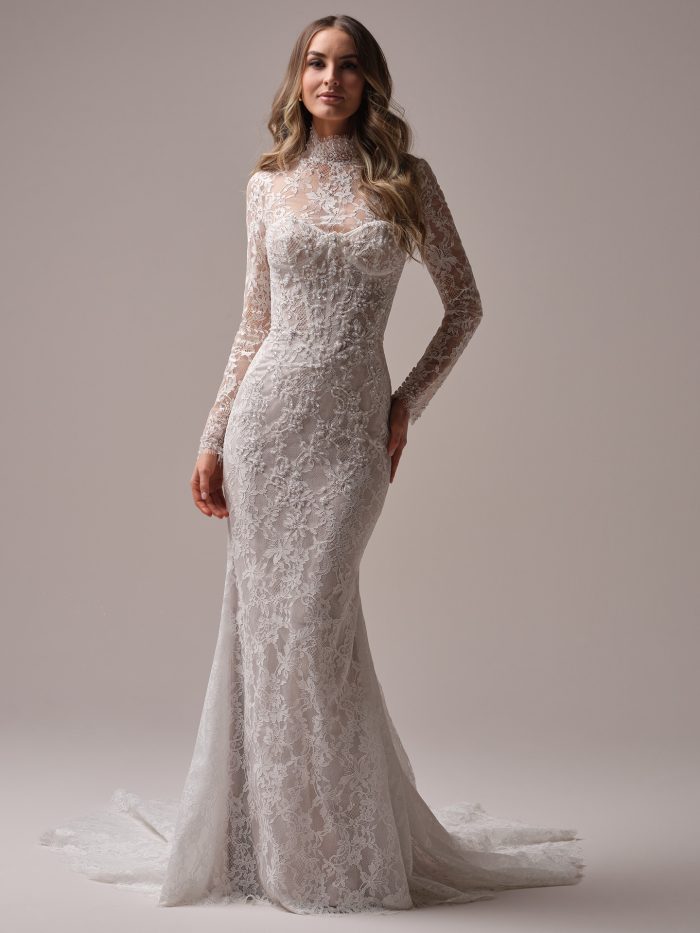 Front view of Sottero and Midgley Jovienne sheath wedding dress featuring allover lace, high illusion neckline, long sleeves, and a subtle sweep train.