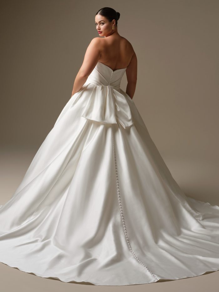Back view of Kincaid by Sottero and Midgley featuring a strapless satin ball gown silhouette with an embellished bow and pearl buttons trailing down the skirt.