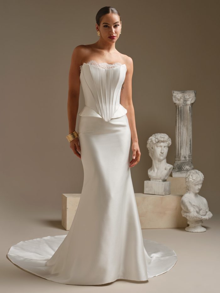 Full-length view of the Lassen Marie sheath satin wedding dress by Sottero and Midgley featuring a strapless corset bodice with lace trim, sculpted peplum detail, and a sleek satin skirt with a subtle train.