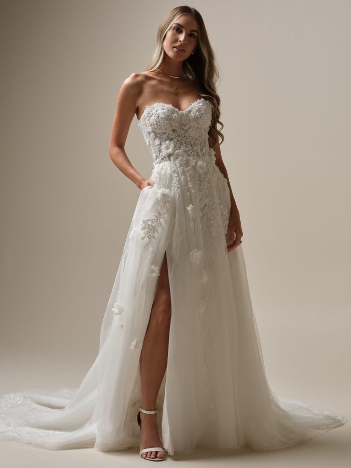 Bride wearing a strapless lace A-line wedding dress with a sweetheart neckline, 3D floral appliqués, thigh-high slit, and chapel train, styled with simple gold jewelry.