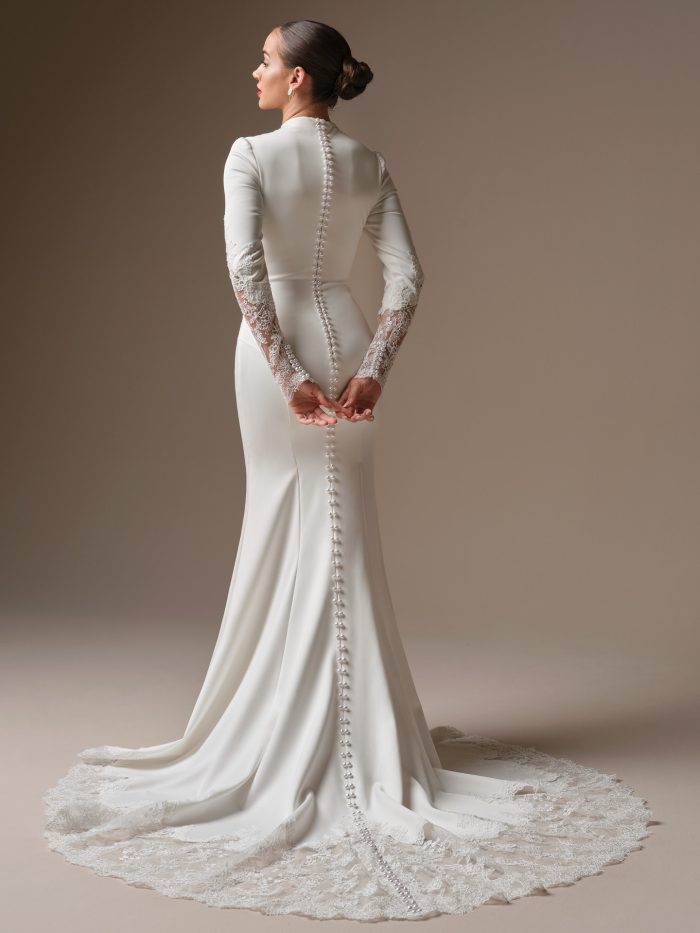 Back view of the Lovai sheath wedding dress by Sottero and Midgley showcasing a pearl button closure down the back, fitted long lace sleeves, and an extended illusion lace train.