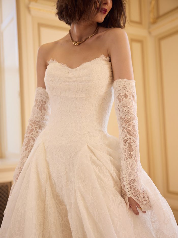 Close-up of the Sottero and Midgley Tamar wedding dress showcasing the strapless lace bodice, sweetheart neckline, and detachable sheer lace sleeves with button accents.