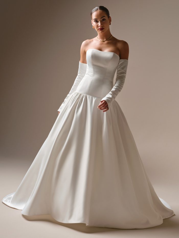 Model wearing the Tokyo wedding dress, a modern satin ball gown featuring a structured strapless bodice, dramatic off-the-shoulder sleeves, and a full gathered skirt for a clean, elevated silhouette.