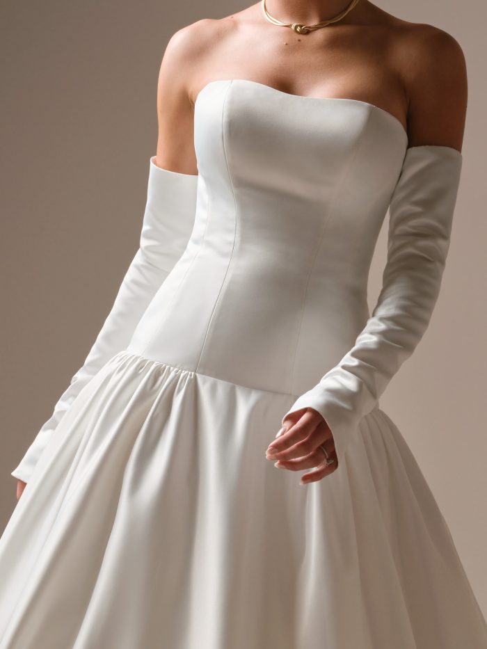 Close-up of the Tokyo wedding dress highlighting the smooth satin strapless bodice, fitted seams, and detachable off-the-shoulder sleeves paired with a voluminous gathered skirt.