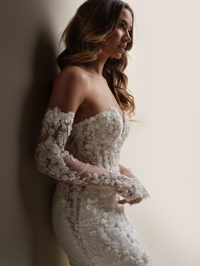 Close-up side view of the Sottero and Midgley Twilight wedding dress showing off-the-shoulder illusion lace sleeves, sheer corset bodice with exposed boning, and sparkling 3-D floral lace motifs with sequins and beads.