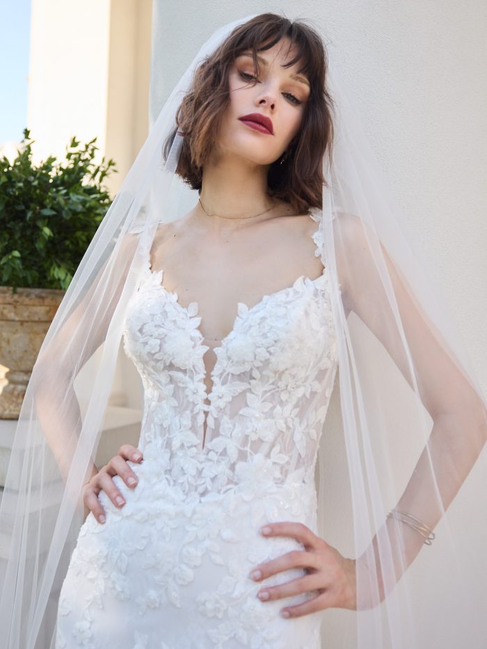 Close-up of the West wedding dress featuring a deep illusion neckline, delicate floral lace appliqués, and thin straps, paired with a long tulle veil.