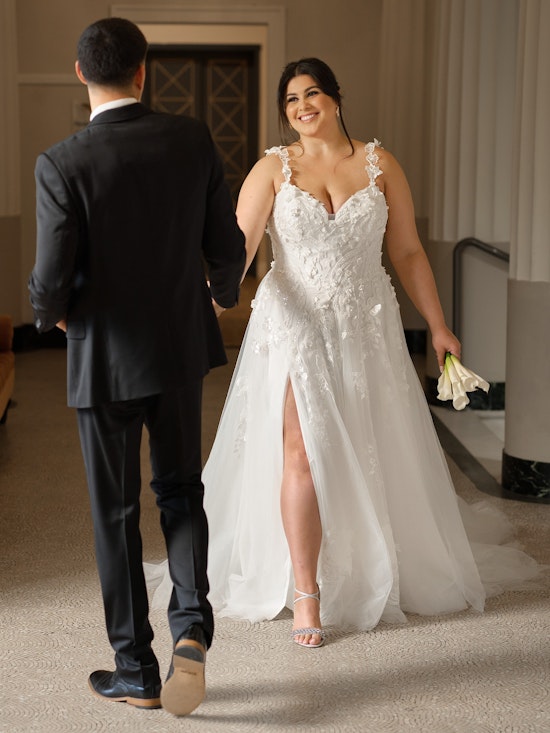 Bride holding groom's hand and walking toward him in a floral wedding dress with a high slit