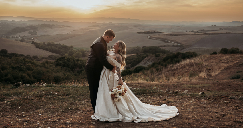 Bride wearing sparkly ballgown wedding dress in the arms of her groom in frontt of a scenic sunset